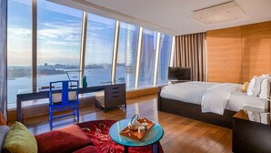 Habitación de hotel con un ventanal grande, cama, escritorio, silla y mesita con bandeja.