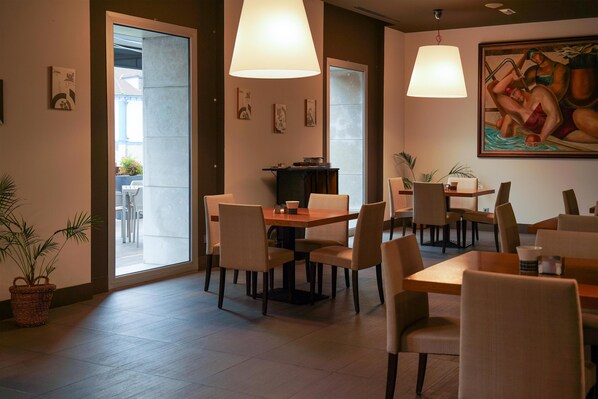 A dining area with tables and chairs, a large painting on the wall, and a potted plant. - Blau Hotel Las Caldas, a member of Radisson Individuals (Oviedo)