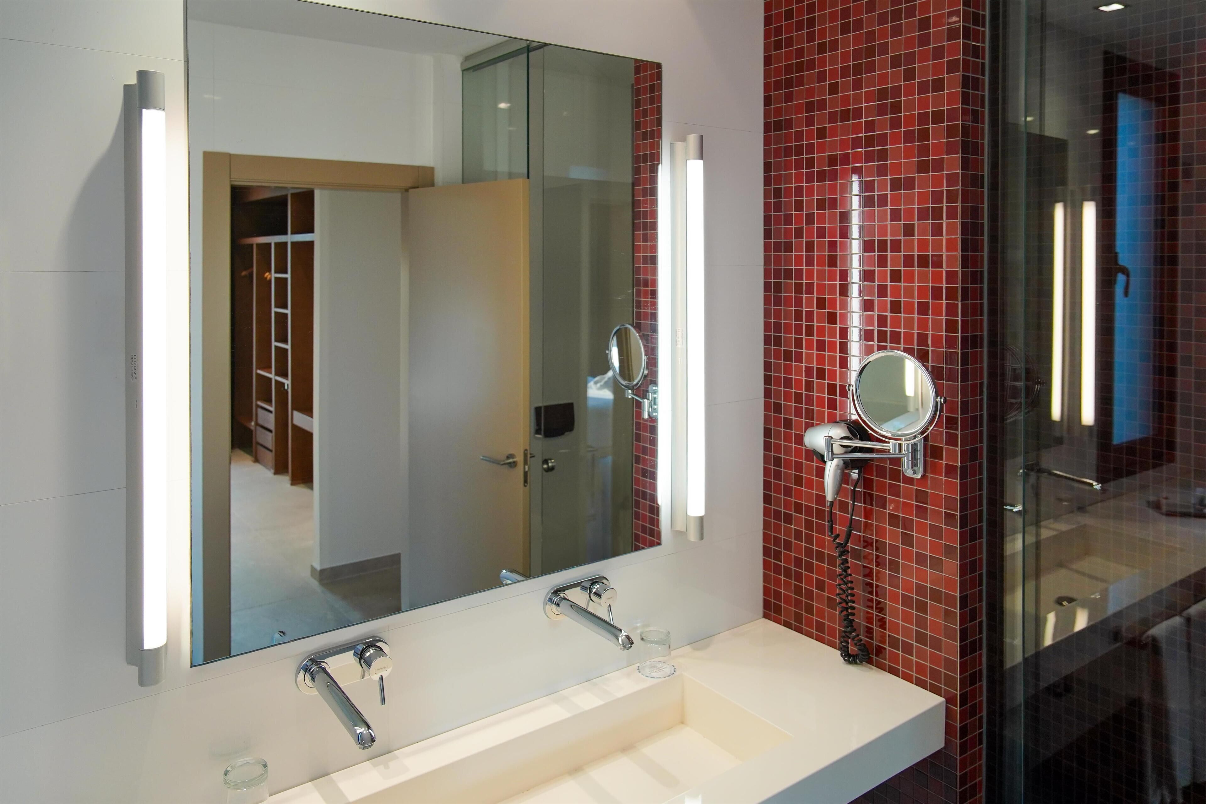 A modern bathroom with a large mirror, a white sink, and red-tiled walls.