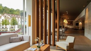 Een moderne hotellobby met een bank, een houten salontafel en een stoel. Grote ramen bieden uitzicht op de stad.