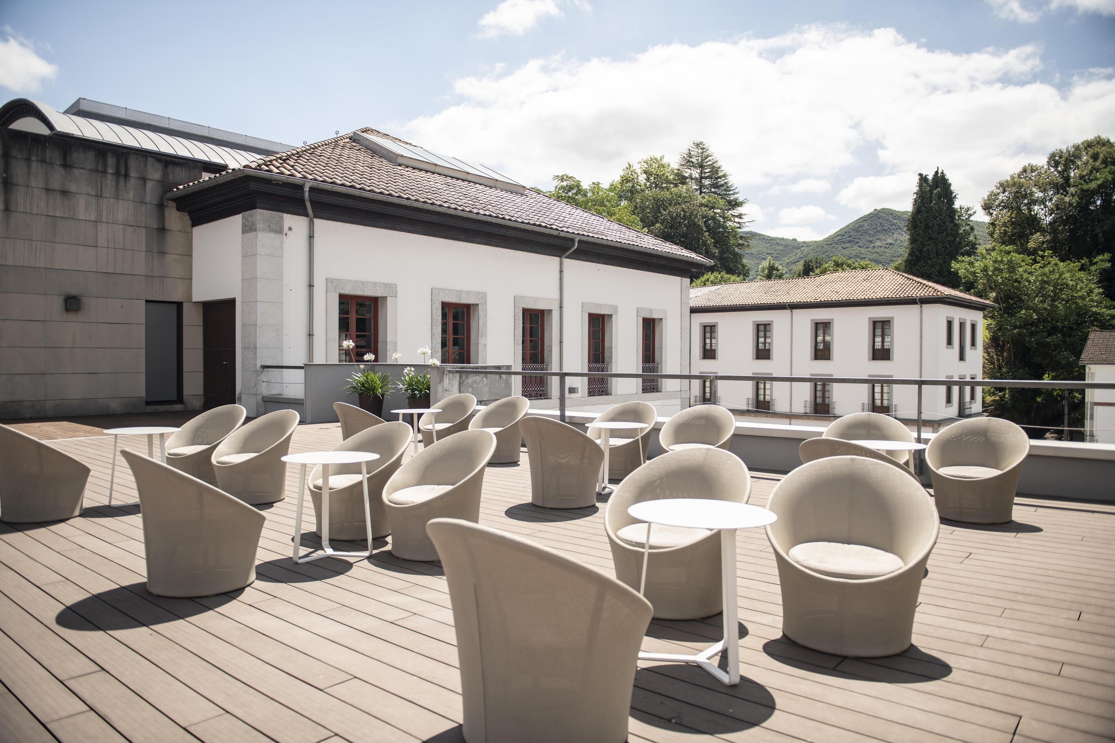 Eine Dachterrasse mit moderner Sitzgelegenheit und Blick auf ein weißes Gebäude mit einem Ziegeldach.