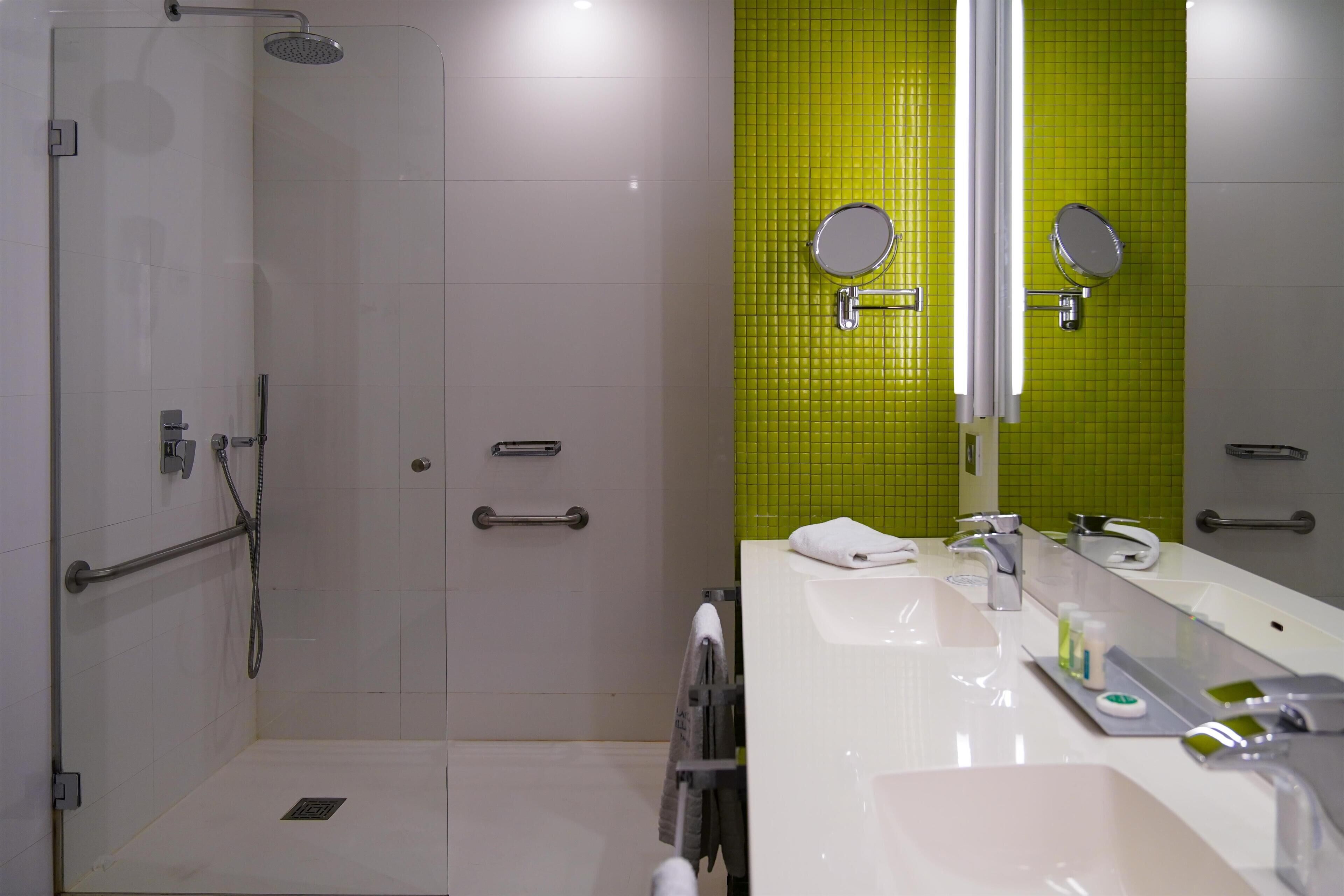 Un baño moderno con cabina de ducha, un espejo grande y un lavamanos blanco con mueble.