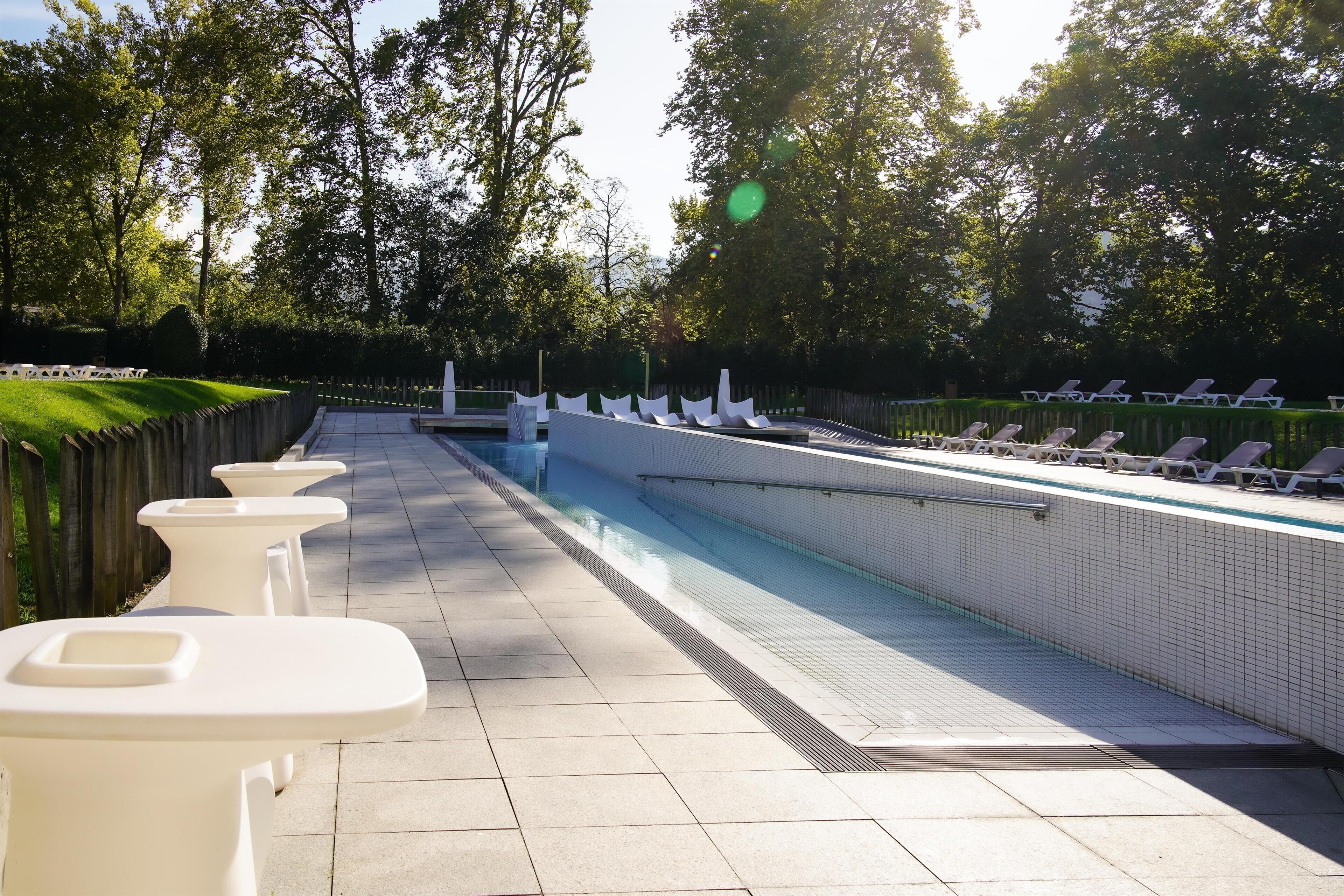 A swimming pool with lounge chairs and white tables along the edge.