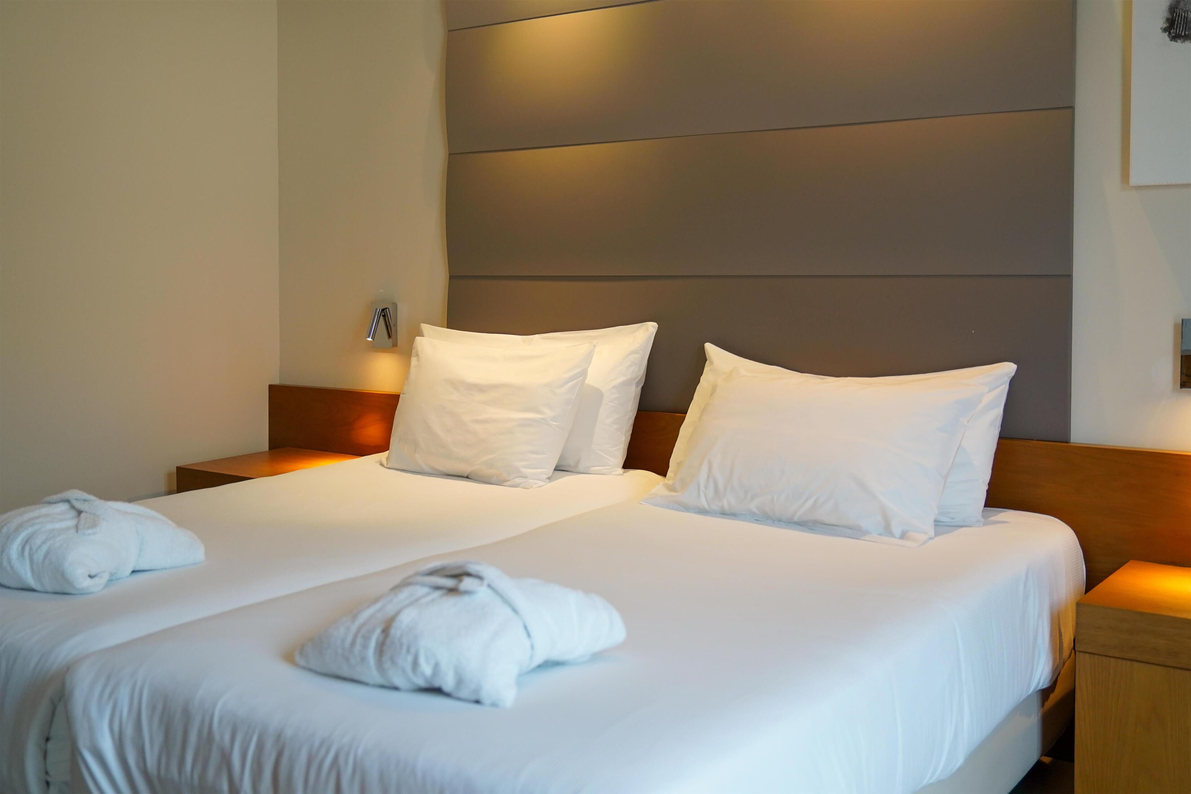 Une chambre d’hôtel avec deux lits, chacun doté de draps et d’oreillers blancs, et d’une tête de lit en bois.