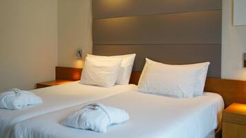 Une chambre d’hôtel avec deux lits, chacun doté de draps et d’oreillers blancs, et d’une tête de lit en bois.