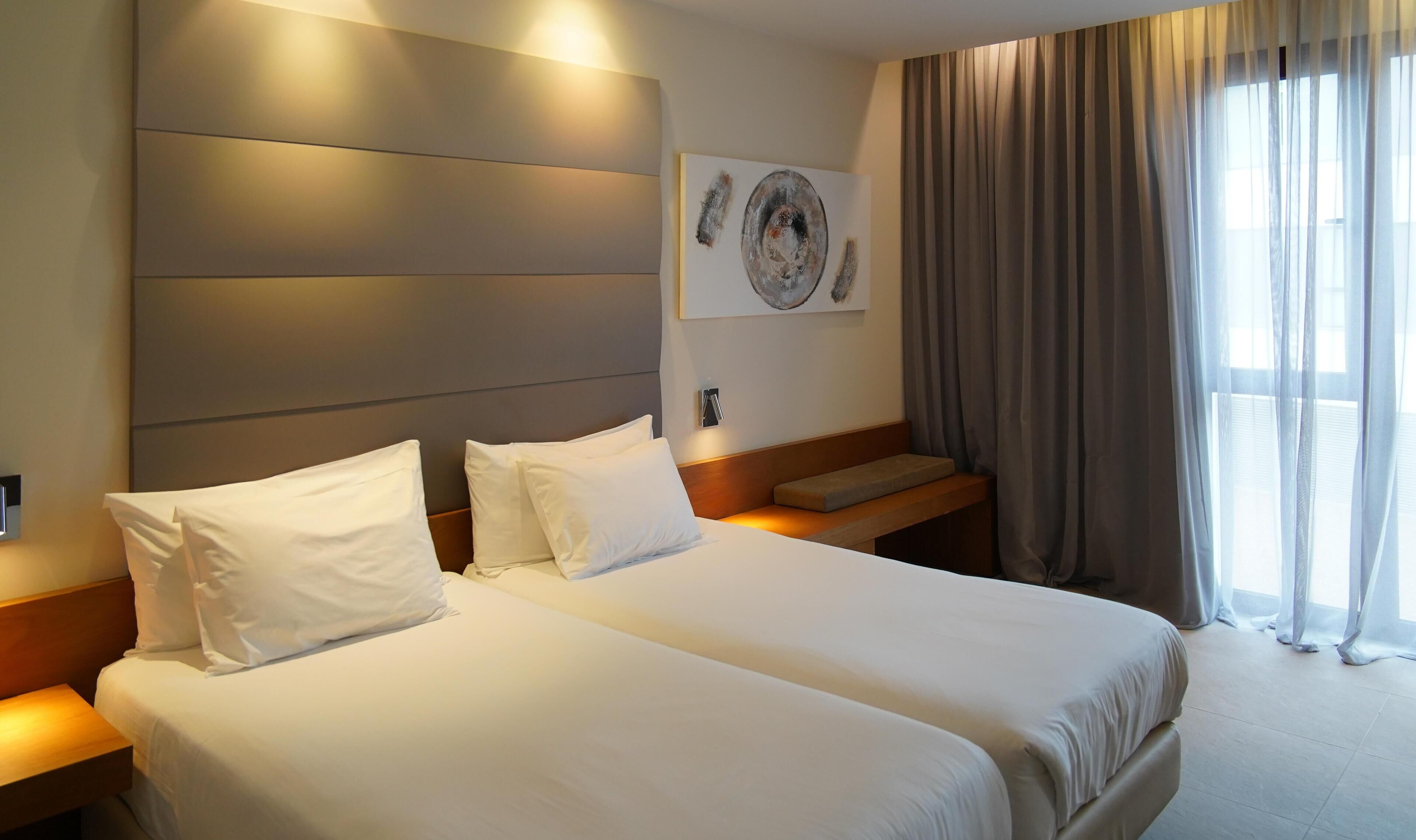 Une chambre d’hôtel avec un grand lit, une table de chevet, une lampe fixée au mur et une fenêtre avec des rideaux.