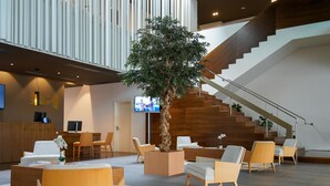 Een moderne lobby met een receptiebalie, een zithoek, een trap en een grote binnentuin.