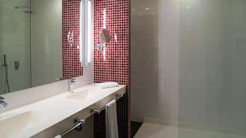 A modern bathroom with a large mirror, two sinks, a glass shower enclosure, and red-tiled walls.