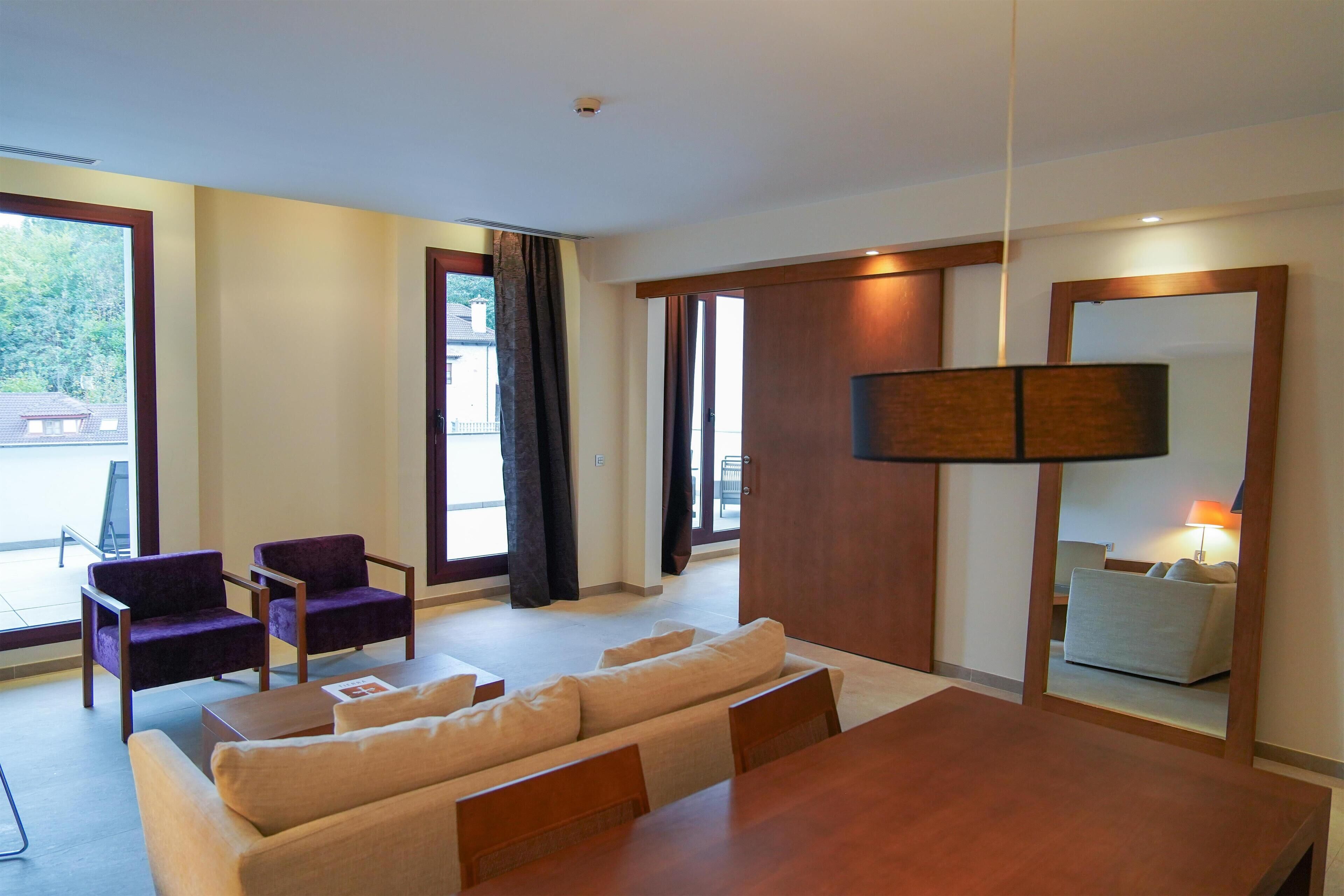 Una sala de estar moderna con un sofá, dos sillones, una mesa de comedor de madera y un espejo grande.