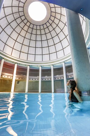 An indoor swimming pool with a glass ceiling and columns. - Blau Hotel Las Caldas, a member of Radisson Individuals (Oviedo)