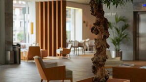 Een moderne lobby met een houten receptiebalie, zachte zitplaatsen en een grote plant.