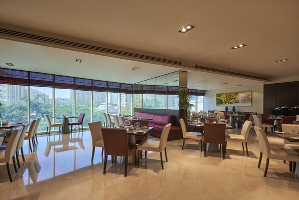 A spacious dining area with high ceilings, large windows, and modern furniture. - Safir Hotel Doha (Doha)