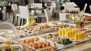 Un bufé con diversos platos y bebidas, incluyendo ensaladas, carnes y frutas, en un comedor bien iluminado con mesas y sillas.