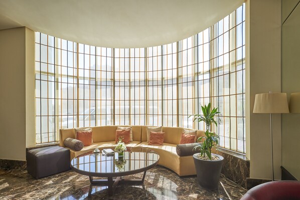 A modern lobby with a curved sofa, a round glass coffee table, and a large window with a grid pattern.