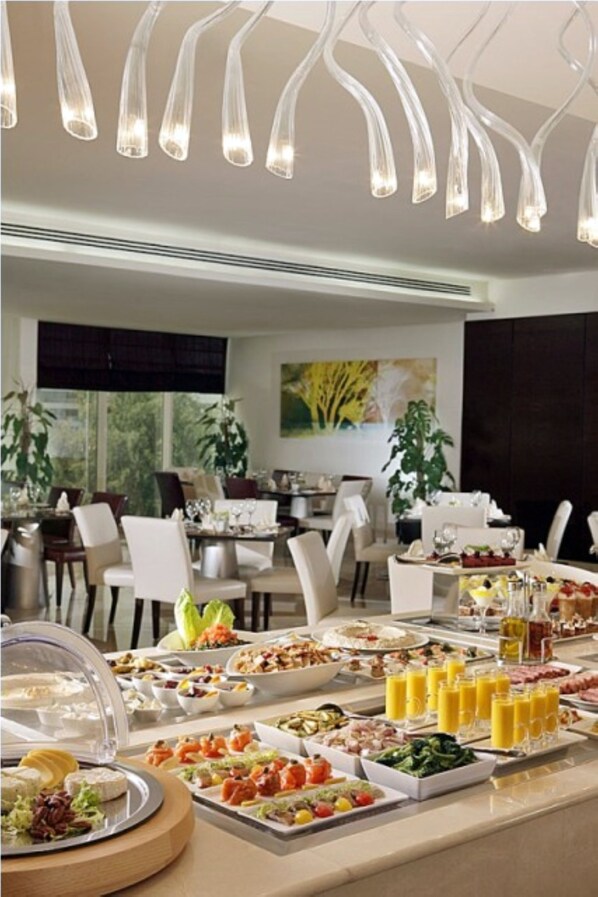 Una mesa de buffet con diferentes alimentos y bebidas, una lámpara moderna de araña y un comedor con sillas y mesas.