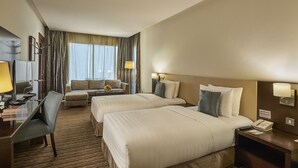 Habitación de hotel con dos camas, un escritorio, una silla, un sofá y vistas al exterior.