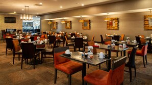 A hotel dining area with multiple tables and chairs, a bar in the background, and a flat-screen TV mounted on the wall. - Holiday Inn Amarillo West Medical Center by IHG (Amarillo)