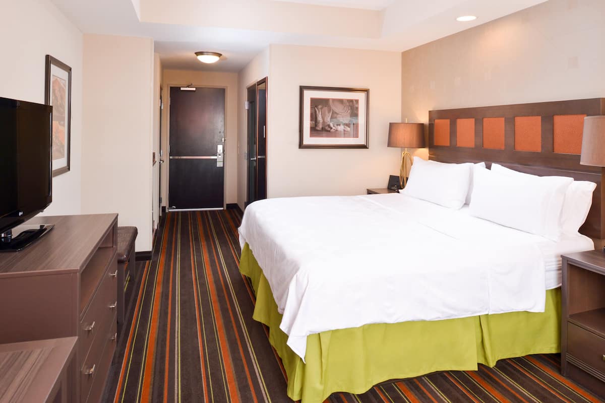 A hotel room with a bed, a TV, a desk, and a door leading to another room.