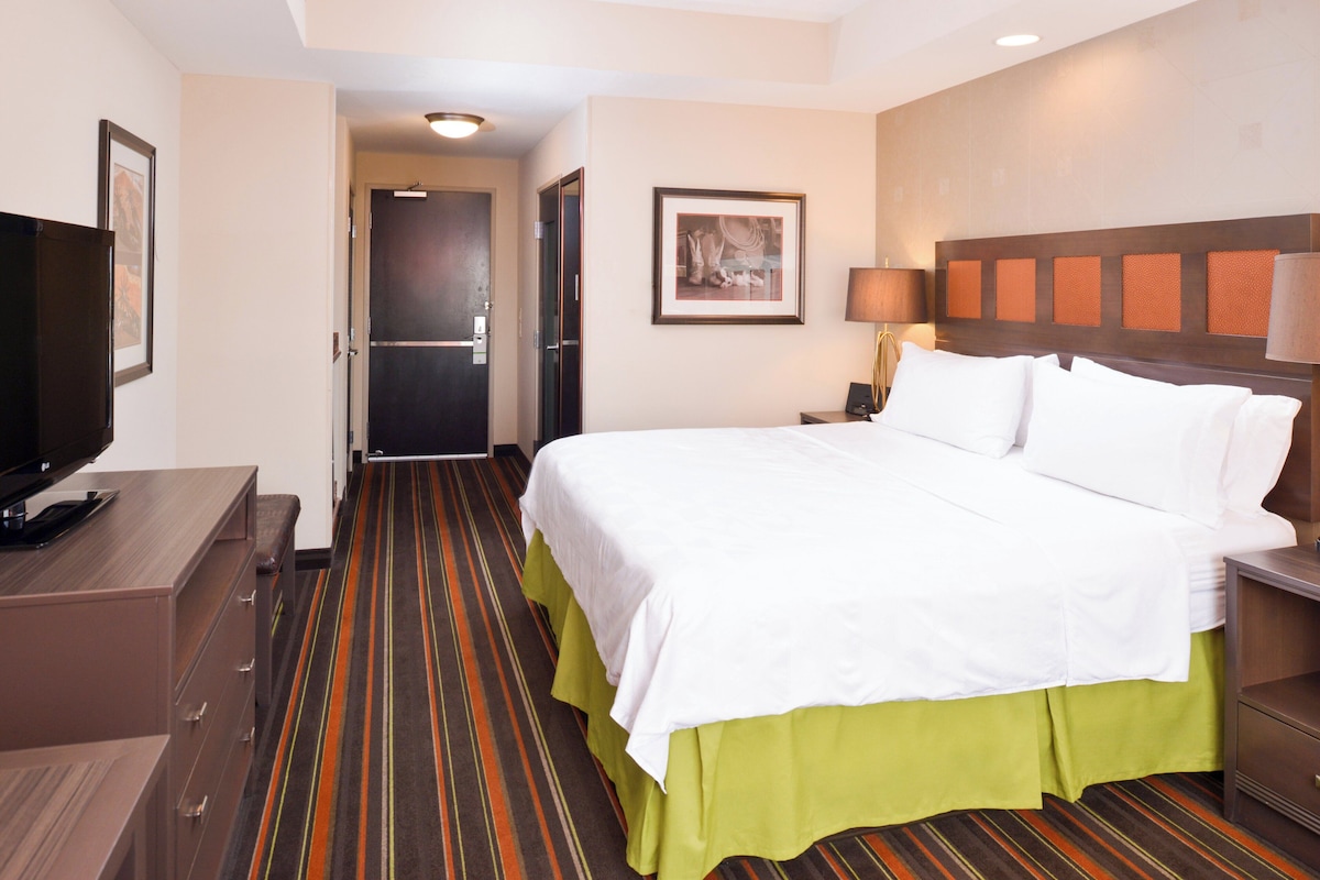 Ein Hotelzimmer mit Bett, Fernseher, Schreibtisch und einer Tür zu einem weiteren Raum.