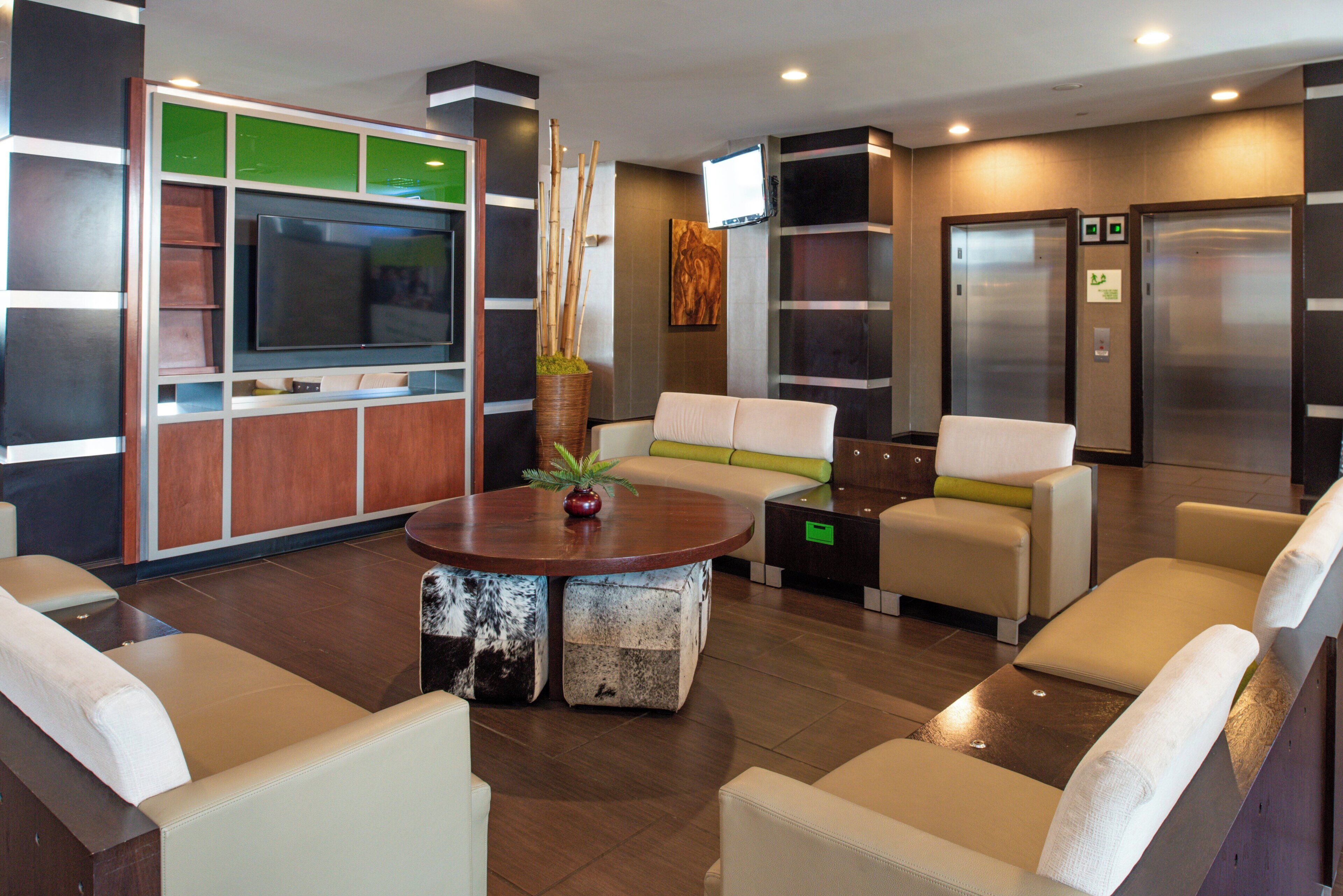 A modern lobby with a flat-screen TV, seating area, elevator, and a reception desk.