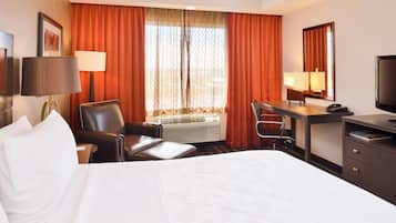 A hotel room with a bed, a desk, a chair, a TV, and an air conditioning unit.