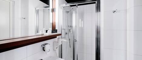 A modern bathroom with a glass-enclosed shower, a white sink, and a mirror with a wooden countertop.