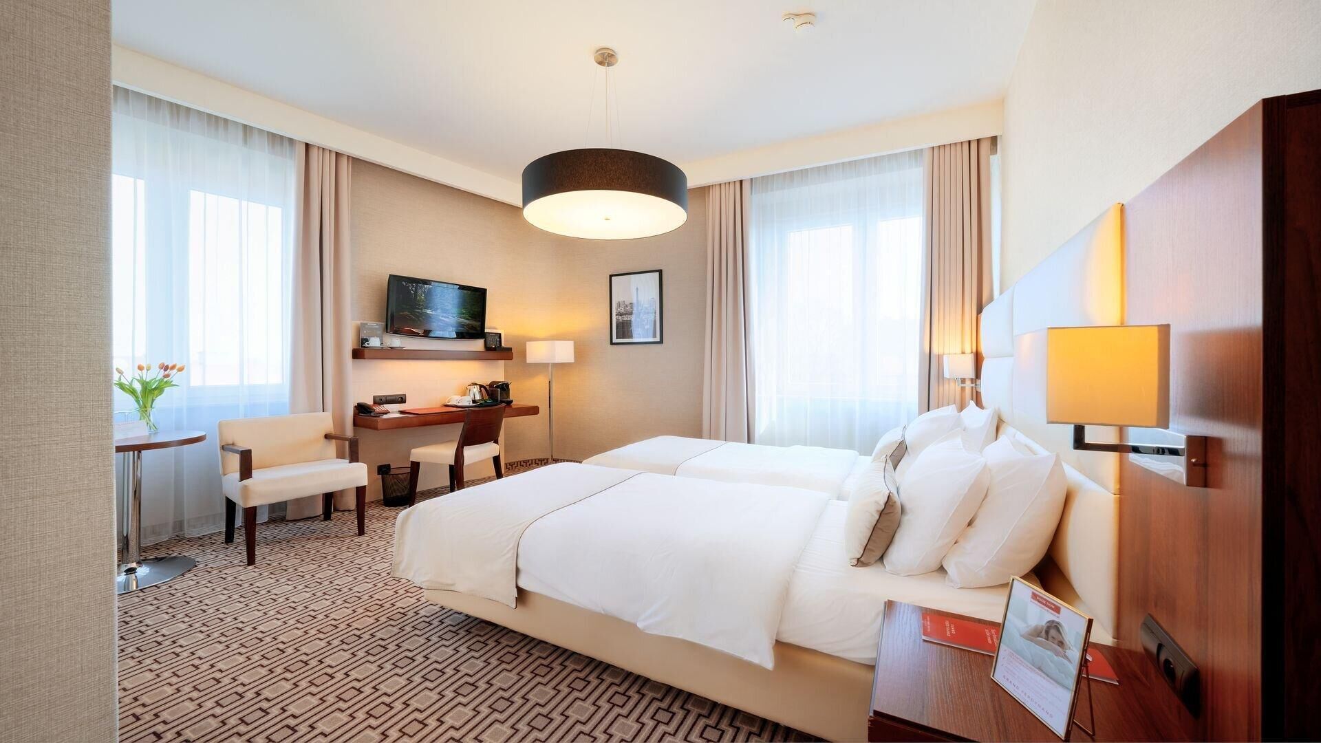 Een hotelkamer met een groot bed, een bureau met stoel, een televisie en een raam met gordijnen.