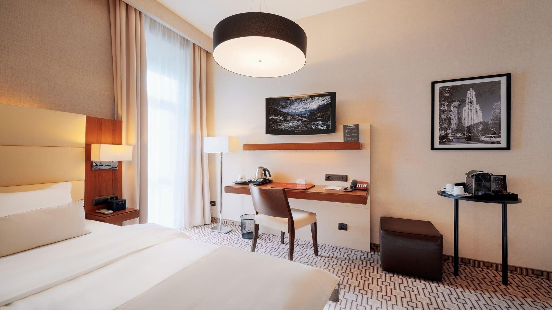 Une chambre d’hôtel avec un grand lit, un bureau avec une chaise, une machine à café et un tableau encadré au mur.