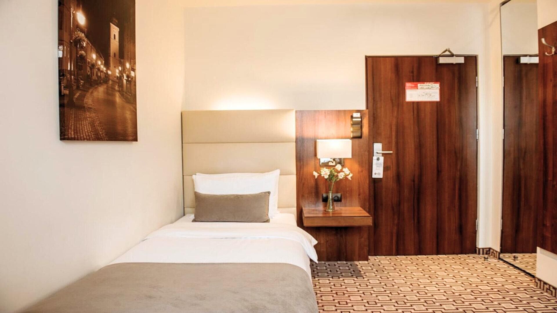A hotel room with a bed, bedside table, lamp, and a wooden door.