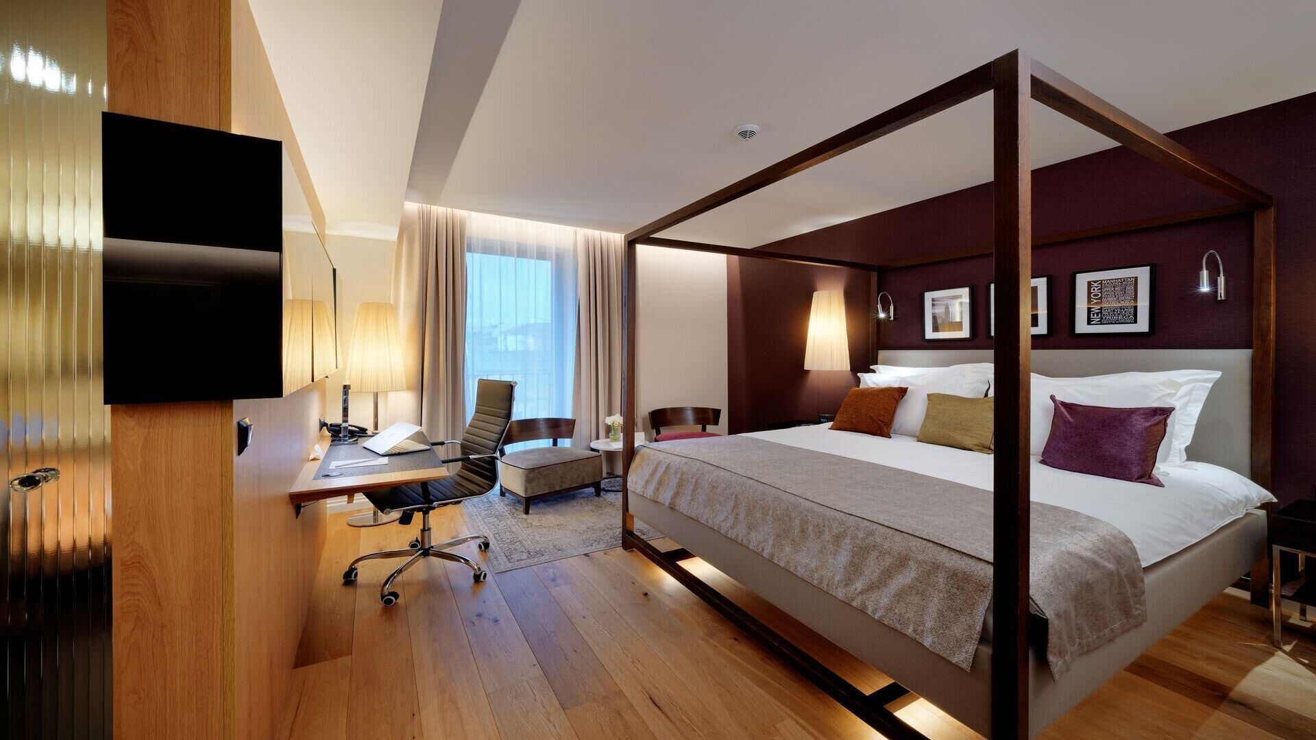 Een moderne hotelkamer met een hemelbed, een bureau met stoel, een flatscreen televisie en een groot raam met gordijnen.