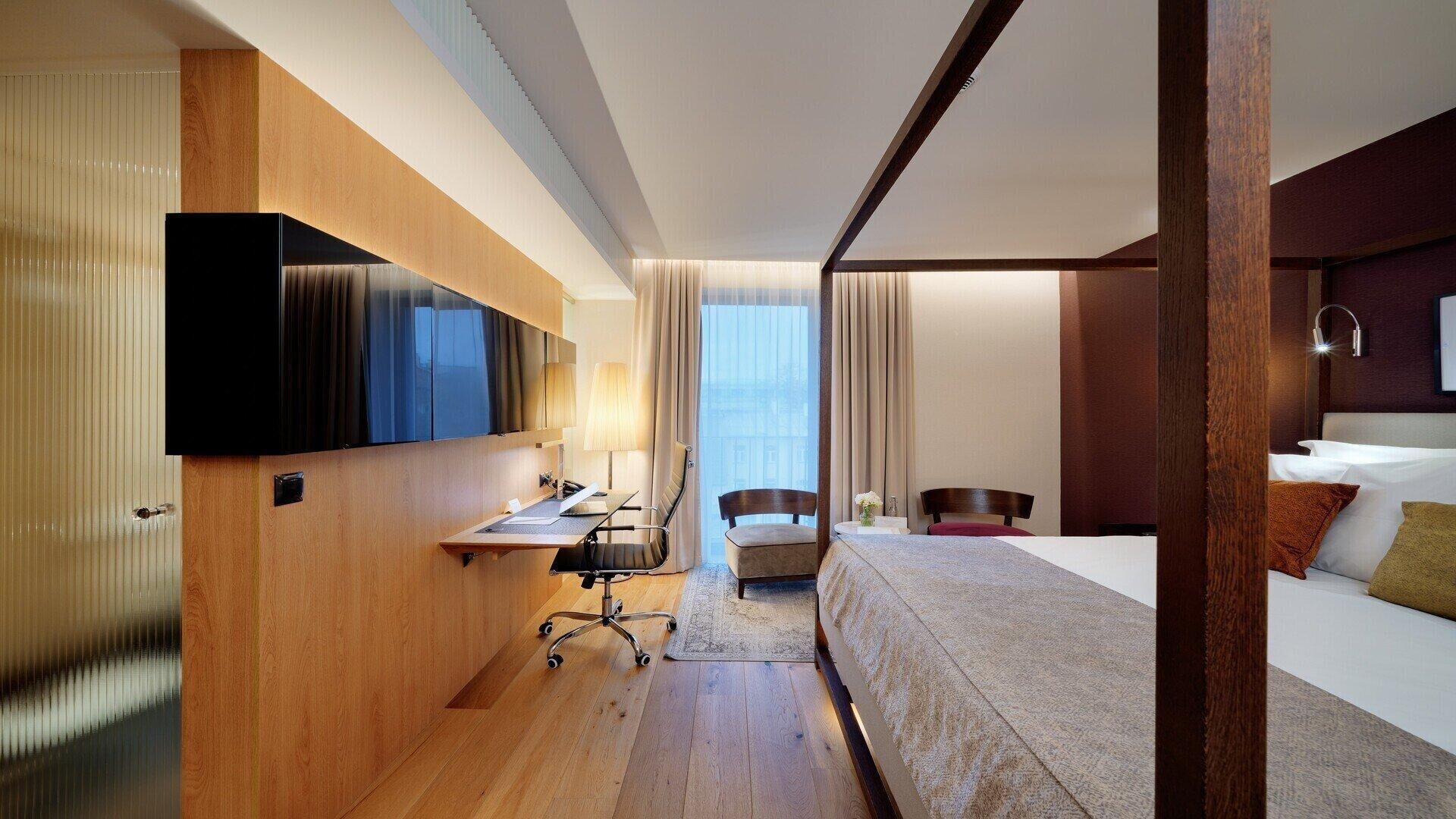 A hotel room with a bed, a desk with a chair, a television, and a window with curtains.