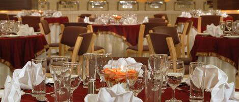 A dining area with tables set for service, featuring red tablecloths, white napkins, and clear glassware.