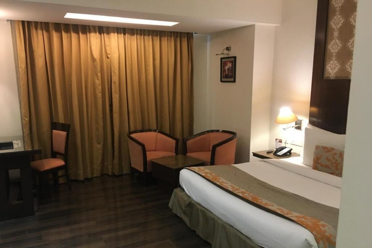 A hotel room with a bed, two chairs, a desk, a lamp, and a telephone.