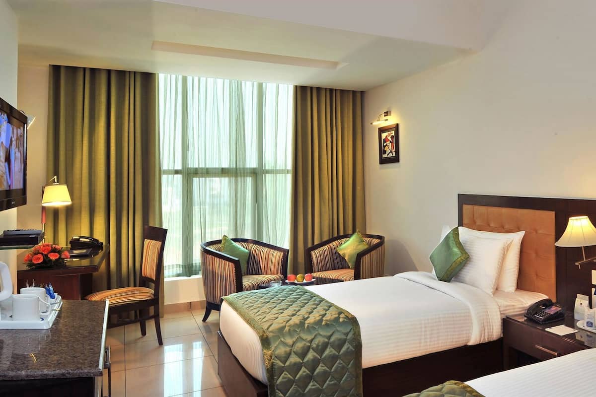 A hotel room with two beds, a desk, a TV, and a large window with curtains.