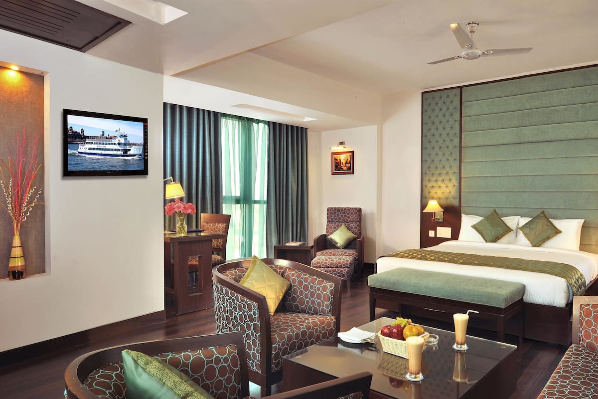 A hotel room with a bed, two armchairs, a sofa, a coffee table, a TV, and a large window with curtains.