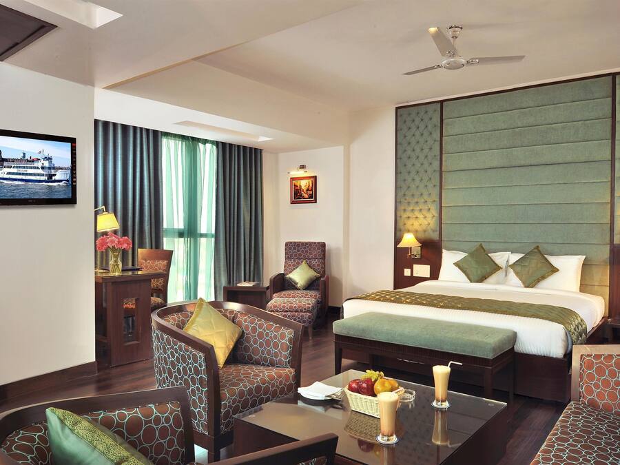 A hotel room with a bed, two armchairs, a sofa, a coffee table, a TV, and a large window with curtains.