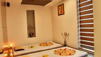 Un cuarto de spa con dos camillas de masaje, velas y un cuenco decorativo en el suelo.