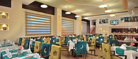 A restaurant with multiple dining tables and chairs, large windows with blinds, and a modern ceiling design.