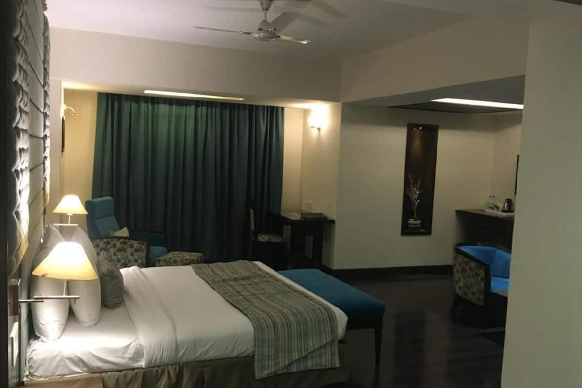 A hotel room with a bed, a desk, a chair, a ceiling fan, and a wall-mounted light fixture.
