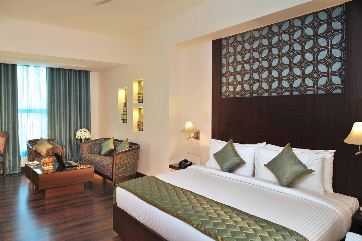 A hotel room with a bed, two armchairs, a desk, and a large window with curtains.