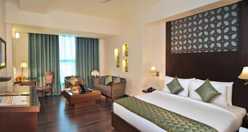 Habitación de hotel con cama, dos sillones, escritorio y un ventanal con cortinas.