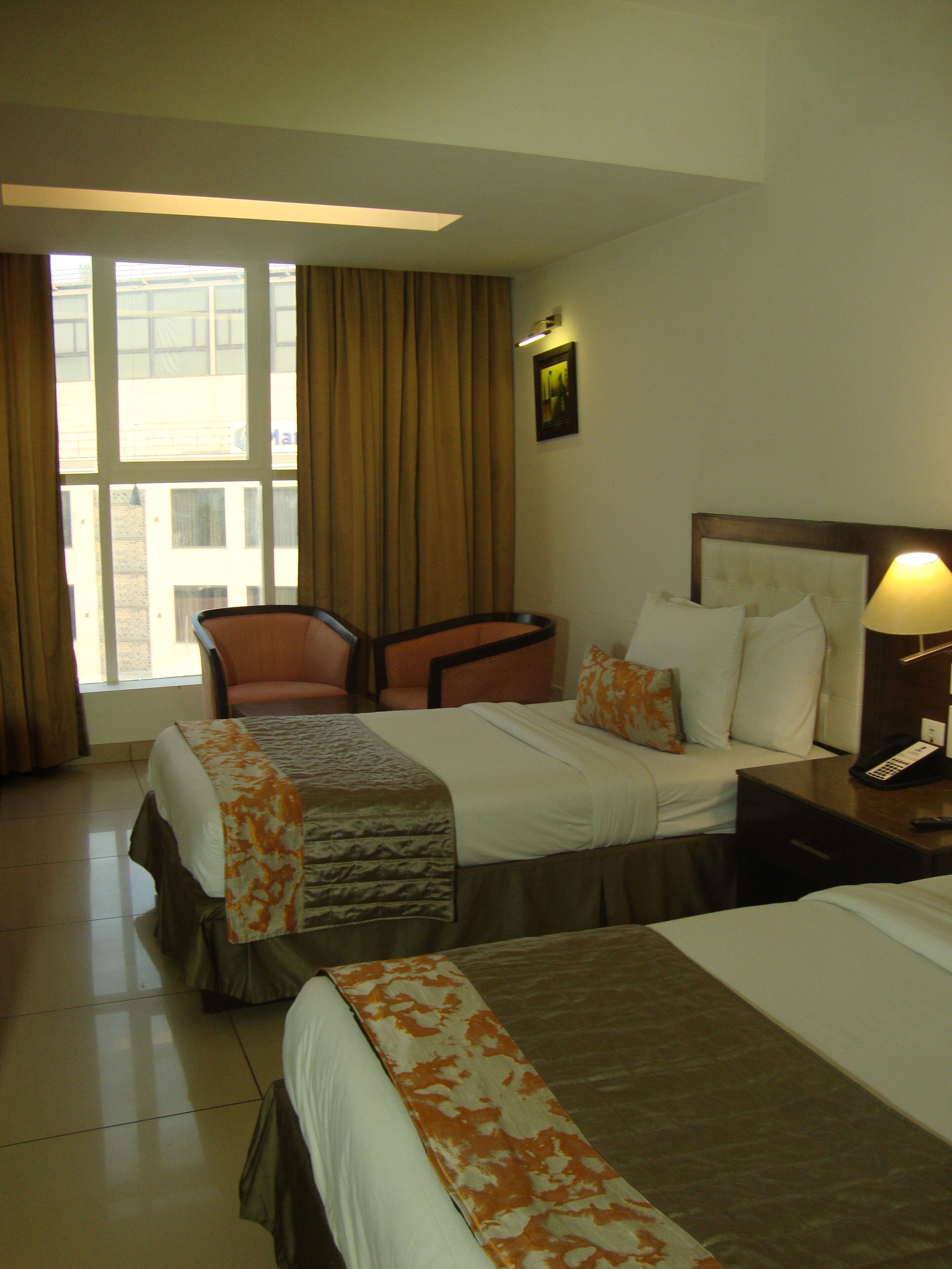 A hotel room with two beds, a chair, a nightstand with a lamp, and a window with curtains.