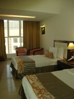 Habitación de hotel con dos camas, una silla, una mesita de noche con lámpara y una ventana con cortinas.