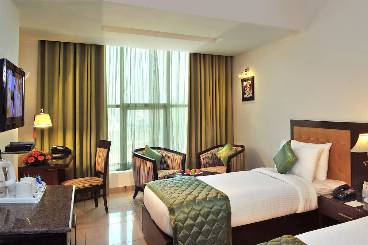 A hotel room with a bed, two chairs, a desk, a TV, and a window with curtains.