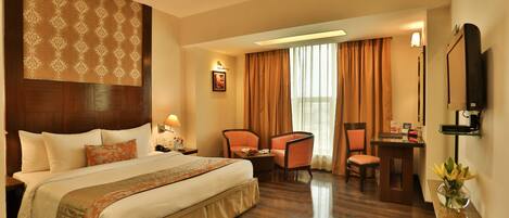 A hotel room with a large bed, a desk, a chair, a TV, and a ceiling fan.