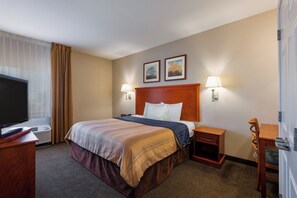 A hotel room with a large bed, two bedside lamps, a flat-screen TV, a desk with a chair, and two framed pictures on the wall. - Candlewood Suites Decatur Medical Center by IHG (Decatur)