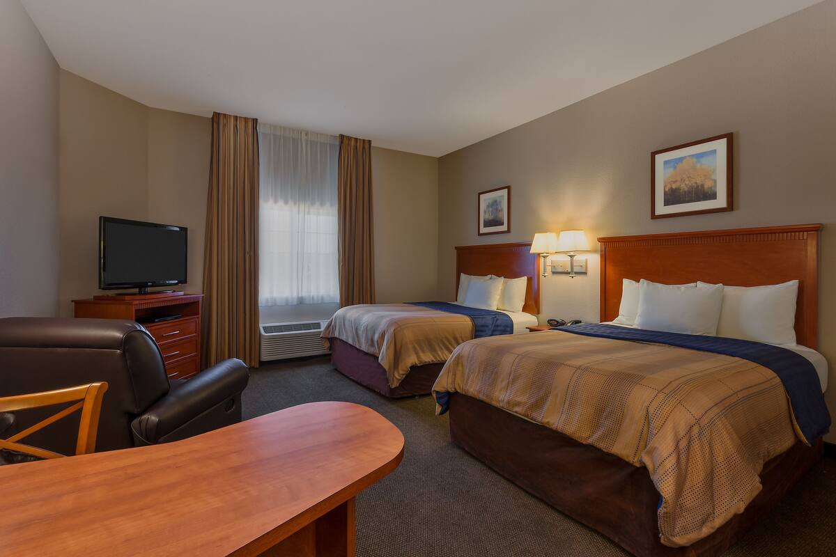 A hotel room with two beds, a desk, a chair, a television, and a window with curtains.