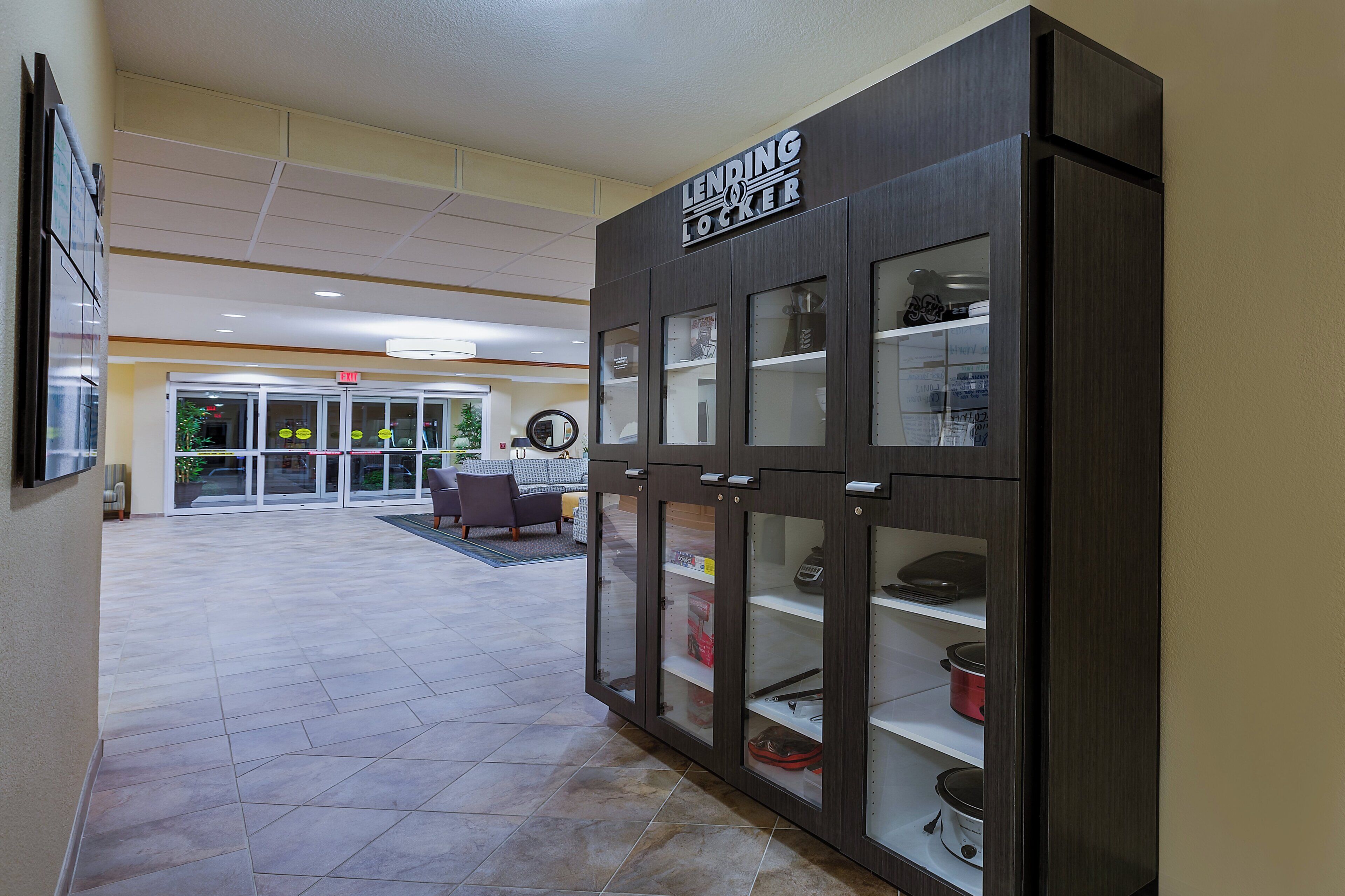 A hotel lobby with a dark wooden reception desk, glass display cabinets, and a seating area with a sofa and chairs.