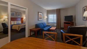 A hotel room with a bed, a blue sofa, a TV, a desk, and a dining table. - Candlewood Suites Decatur Medical Center by IHG (Decatur)