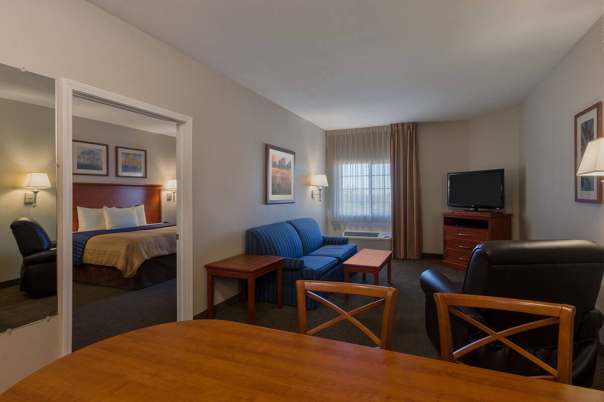 A hotel room with a bed, a blue sofa, a TV, a desk, and a dining table.